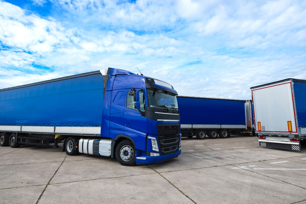 Ein blauer Sattelschlepper steht neben anderen Lastwagen unter einem teilweise bewölkten Himmel auf einem Betonplatz und ist bereit für seine Umzugsreise von Österreich nach Deutschland.